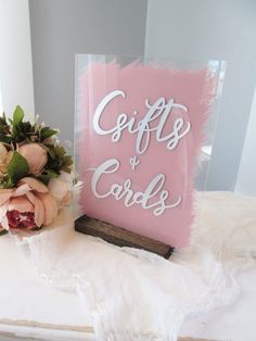 a pink sign that says gifts and cards next to some flowers on a white table