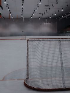 an empty hockey rink with lights on the ceiling and net in the foreground, as seen from across the ice