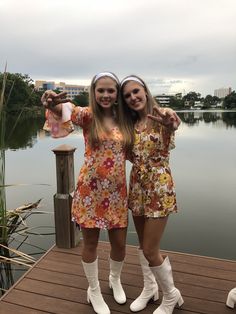 two girls standing on a dock with their arms around each other and pointing at the camera