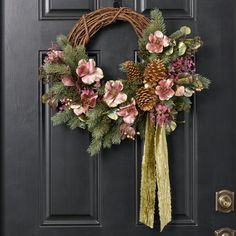 a wreath with pine cones and pink flowers hangs on a black front door decorated with greenery