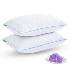 two pillows and a purple flower on a white surface next to the pillow that has been placed