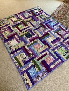 a purple and green patchwork quilt on the floor next to an area rug that has been made into a wall hanging