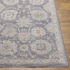 a gray and beige area rug with an ornate design on the center, surrounded by wood flooring