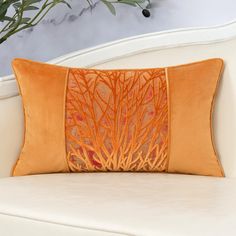 an orange decorative pillow sitting on top of a white couch next to a potted plant