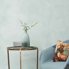 a blue chair next to a small table with a vase on it and a pillow