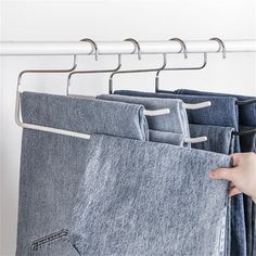 a person is holding three pairs of jeans in front of a rack with clothes hanging on it