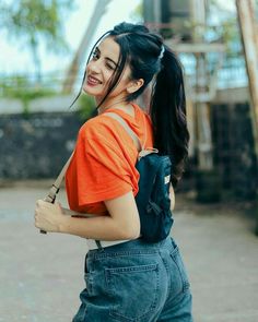 a woman with long black hair wearing an orange shirt and jeans