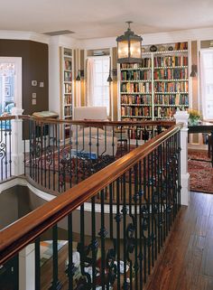 a living room filled with lots of books on top of a book shelf next to a stair case