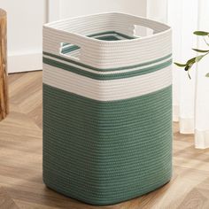 a green and white basket sitting on top of a wooden floor next to a plant