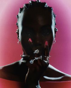 a woman with rings on her fingers posing for a photo in front of a pink background