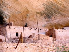 an adobe style building in front of a cliff side with flags and poles sticking out of it