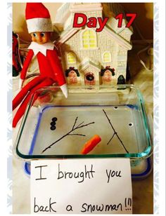 an elf is sitting in front of a glass tray with a sign on it that says, i brought you back a snowman