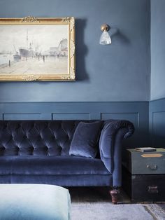 a living room with blue walls and a black velvet couch in front of a painting on the wall