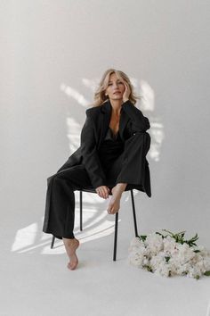 a woman sitting on a chair in front of a white wall with flowers around her