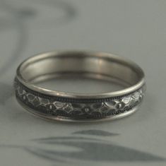 two silver rings with floral designs are sitting on a table top, one is slightly open and the other half has a shadow behind it