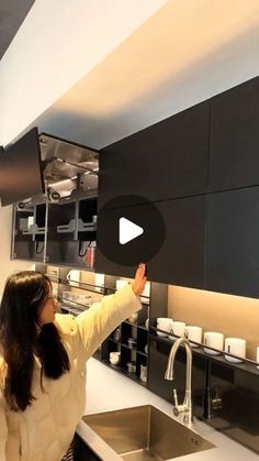 a woman standing in front of a kitchen sink next to a wall mounted faucet