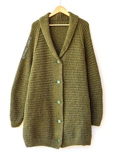 a green cardigan sweater hanging on a wooden hanger with a white wall in the background