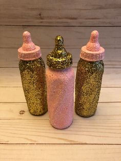 three glitter bottles sitting on top of a white wooden floor next to each other, one pink and one gold