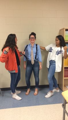 three young women standing in front of a book shelf talking to each other and smiling