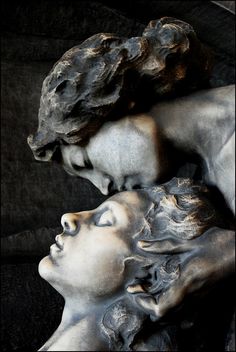 a statue of two women with their heads touching each other's shoulders in front of a black background