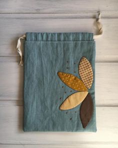 a blue bag with an appliqued flower on the front and brown leaves on the back