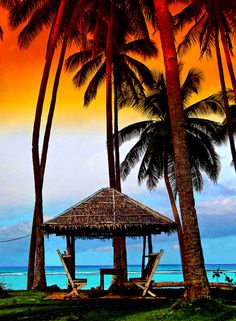 a hut on the beach with palm trees in front of it and an orange sky