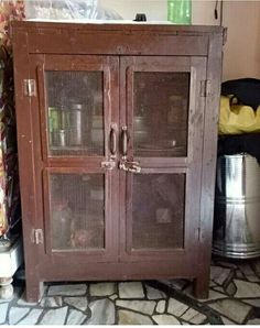 an old wooden cabinet with glass doors on the top and bottom, next to a trash can