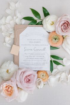 the wedding stationery is surrounded by pink and white flowers, greenery, and brown paper