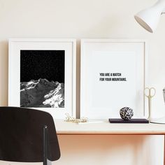 two framed pictures sitting on top of a desk next to a black and white lamp