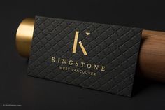 a black business card sitting on top of a rolling pin with gold foil lettering and a wooden handle