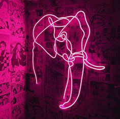 a neon pink elephant head on display in a dark room with comic pages all over the walls