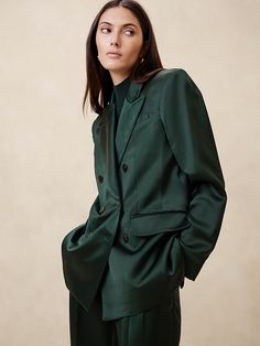 a woman in a dark green suit poses for the camera with her hands on her hips