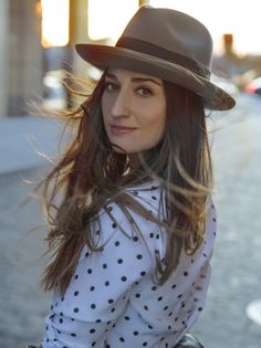 a woman with long hair wearing a black hat and polka dot shirt standing on the street