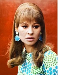 a woman with long hair wearing blue and green polka dot shirt, earrings and looking off to the side