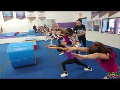 people in a gym doing exercises on the blue mat with one woman holding out her hand