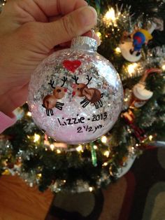 someone holding up a christmas ornament in front of a tree