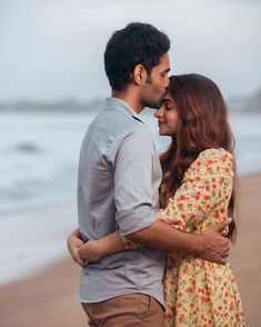 a man and woman standing next to each other on the beach with ocean in background