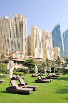 lounge chairs and umbrellas on the lawn in front of tall buildings