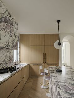 a kitchen with marble counter tops and wooden cabinets, along with stools that match the wood flooring