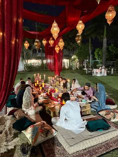 a group of people sitting around a table under a red tent with lights on it