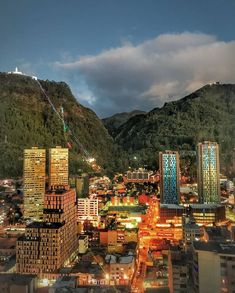 the city is lit up at night with mountains in the background