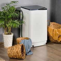 a small white refrigerator sitting next to a potted plant and wicker baskets on the floor