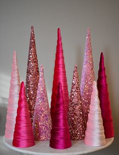 three pink and one white cone shaped trees with sequins on them in front of a gray wall