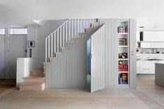 an open staircase leading up to a kitchen with white cabinets and wooden flooring, along with bookshelves