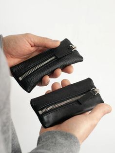 a person holding two black leather wallets in their hands, both with zippers on them