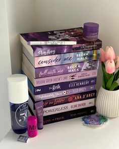 a stack of books sitting on top of a white shelf next to a vase filled with flowers