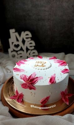 a white cake with pink flowers on it sitting on a gold plated platter