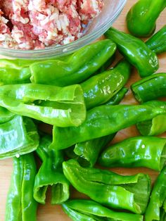 some green peppers are on a wooden table next to a glass bowl with food in it