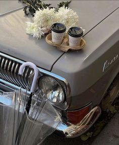 an old car with flowers on the hood and two cups of coffee sitting on top