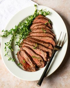 a white plate topped with sliced meat and green garnish next to a fork